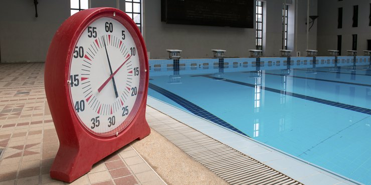 A pace clock for swimming with one red hand that counts the seconds and one black hand that counts the minutes